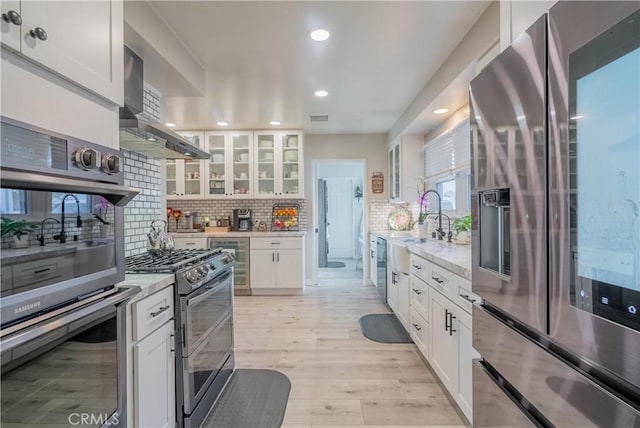 kitchen featuring appliances with stainless steel finishes, white cabinetry, wall chimney range hood, and light stone countertops