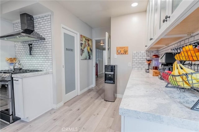 kitchen featuring stainless steel range, white cabinets, wall chimney range hood, and tasteful backsplash