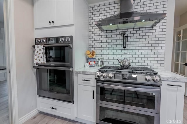 kitchen featuring range with two ovens, double oven, wall chimney exhaust hood, white cabinetry, and tasteful backsplash