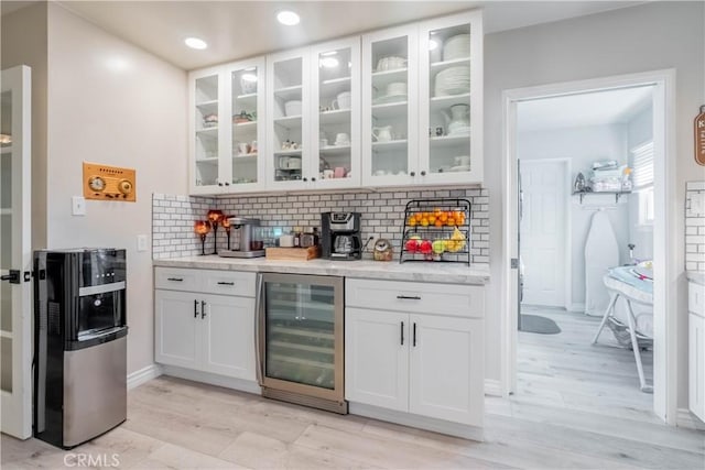 bar featuring white cabinetry, tasteful backsplash, wine cooler, and light stone countertops