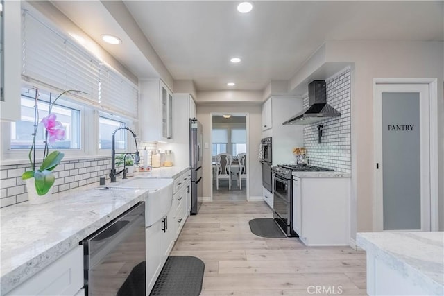 kitchen with appliances with stainless steel finishes, light stone counters, white cabinets, wall chimney range hood, and backsplash