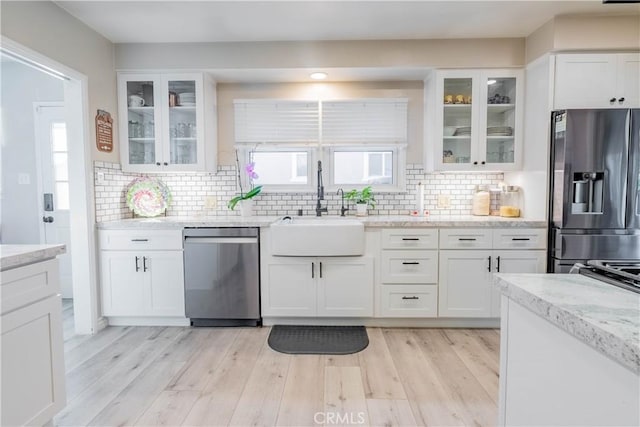 kitchen with stainless steel appliances, sink, white cabinetry, light hardwood / wood-style floors, and tasteful backsplash