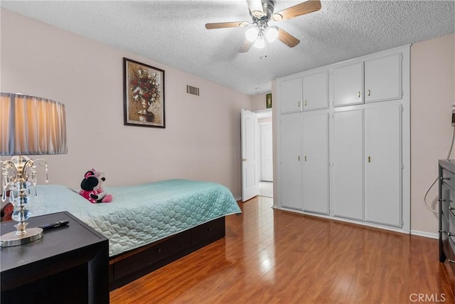 bedroom with ceiling fan, light hardwood / wood-style floors, a closet, and a textured ceiling