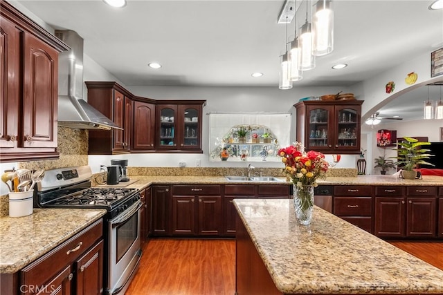 kitchen featuring stainless steel gas range, pendant lighting, wall chimney exhaust hood, sink, and light hardwood / wood-style flooring