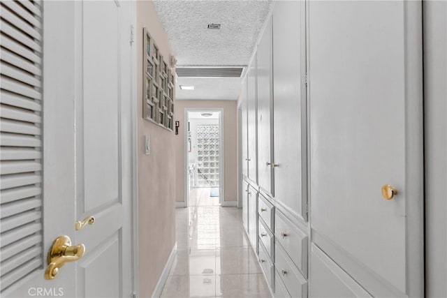 hallway with a textured ceiling and light tile patterned floors