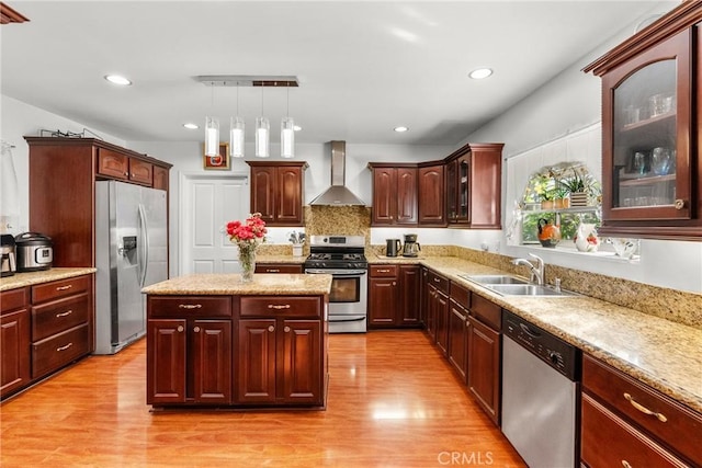 kitchen featuring appliances with stainless steel finishes, hanging light fixtures, light wood-type flooring, sink, and wall chimney range hood