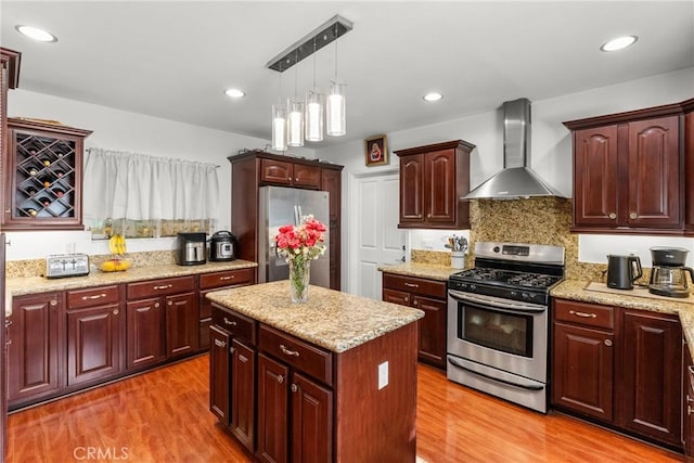 kitchen featuring hardwood / wood-style floors, appliances with stainless steel finishes, hanging light fixtures, a kitchen island, and wall chimney exhaust hood