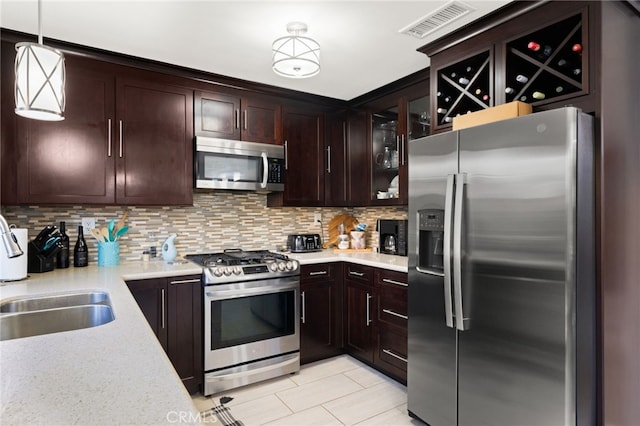 kitchen with appliances with stainless steel finishes, light countertops, decorative light fixtures, and glass insert cabinets