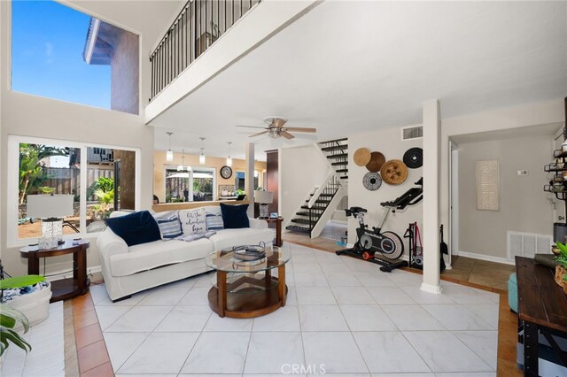 living room featuring light tile patterned flooring, visible vents, ceiling fan, and stairs