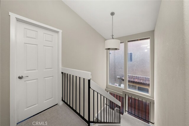 hall with lofted ceiling, plenty of natural light, light colored carpet, and an upstairs landing