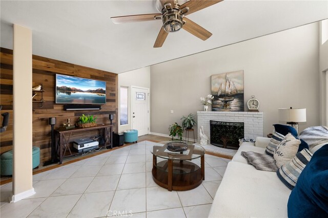 living room featuring light tile patterned floors, ceiling fan, wooden walls, baseboards, and a brick fireplace