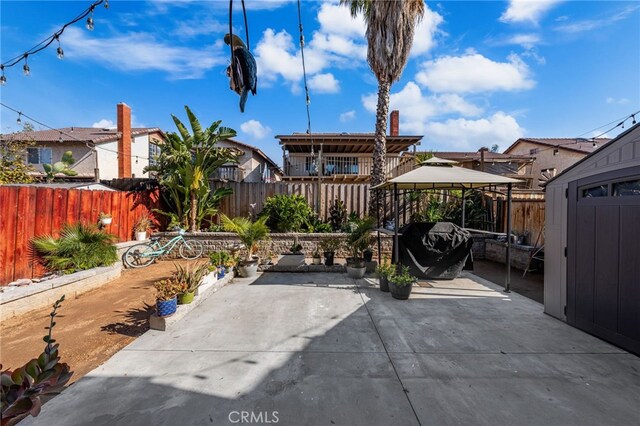 view of patio / terrace with a gazebo, a storage unit, a fenced backyard, and a residential view