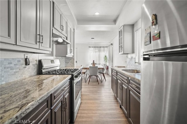 kitchen featuring hanging light fixtures, dark brown cabinets, light stone counters, and stainless steel appliances