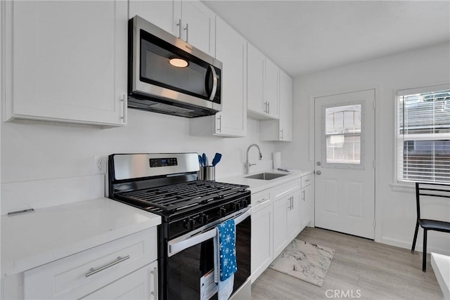 kitchen with white cabinets, stainless steel appliances, a sink, and light countertops