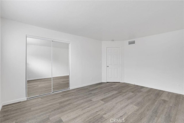 unfurnished bedroom with a closet, wood finished floors, visible vents, and baseboards