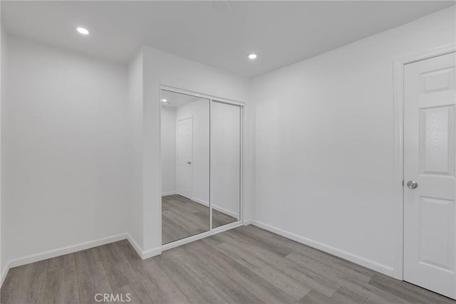 unfurnished bedroom with a closet, baseboards, wood finished floors, and recessed lighting