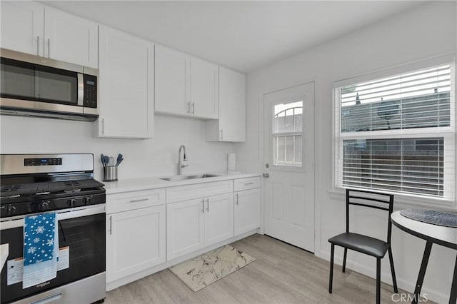 kitchen with appliances with stainless steel finishes, white cabinets, a sink, and light wood-style flooring