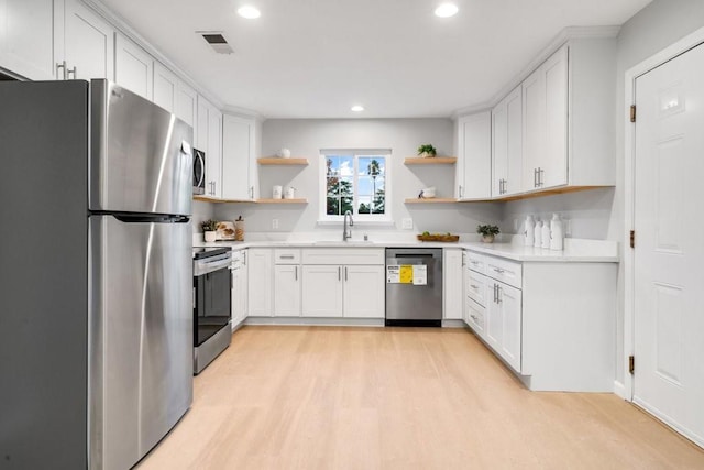 kitchen with appliances with stainless steel finishes, sink, white cabinets, and light wood-type flooring