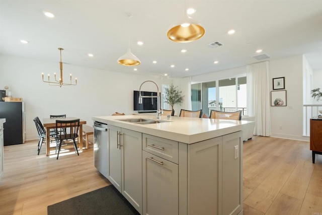 kitchen with decorative light fixtures, a kitchen island with sink, stainless steel dishwasher, and light hardwood / wood-style floors