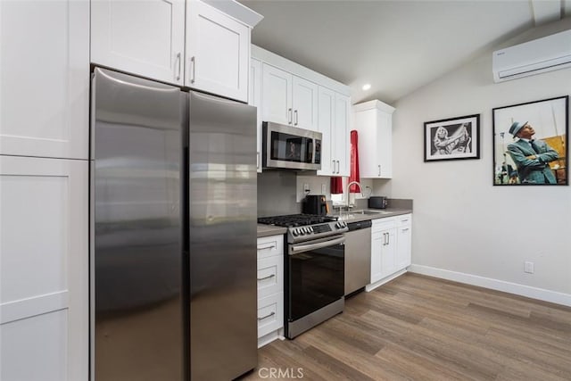 kitchen featuring white cabinetry, appliances with stainless steel finishes, a wall unit AC, and vaulted ceiling