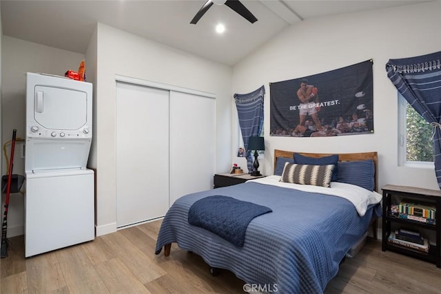 bedroom featuring hardwood / wood-style floors, stacked washer / drying machine, a closet, vaulted ceiling, and ceiling fan