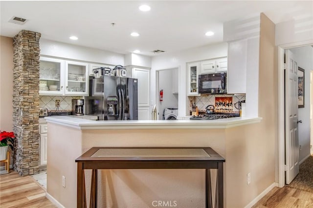 kitchen featuring black appliances, white cabinets, kitchen peninsula, and light hardwood / wood-style flooring