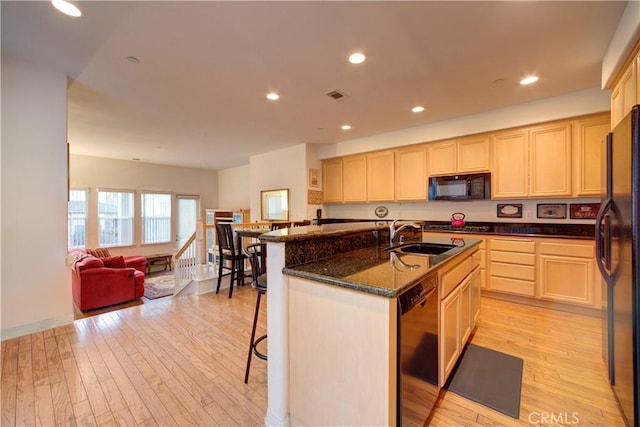 kitchen with sink, light hardwood / wood-style floors, an island with sink, a breakfast bar area, and black appliances