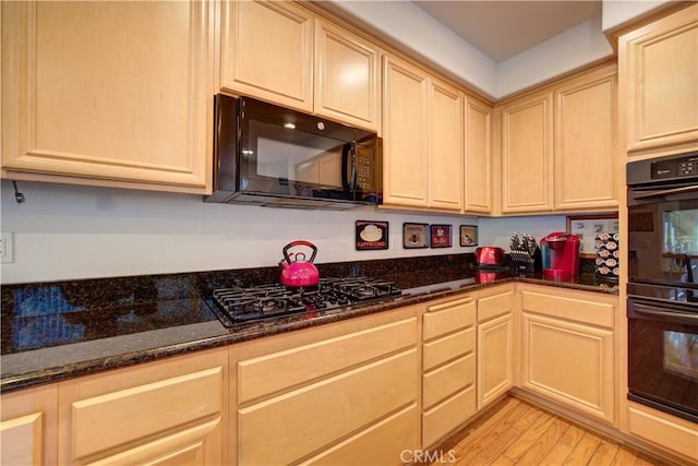 kitchen featuring light brown cabinetry, dark stone countertops, black appliances, and light hardwood / wood-style flooring