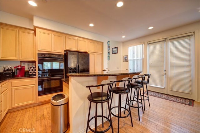 kitchen with a center island, black appliances, dark stone counters, and light hardwood / wood-style flooring