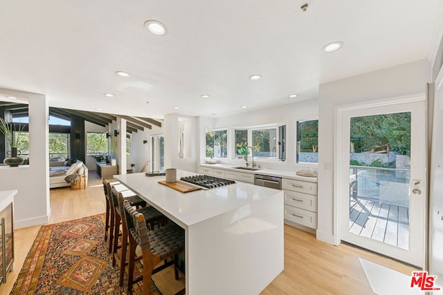 kitchen with light hardwood / wood-style floors, a kitchen island, sink, white cabinetry, and a kitchen breakfast bar