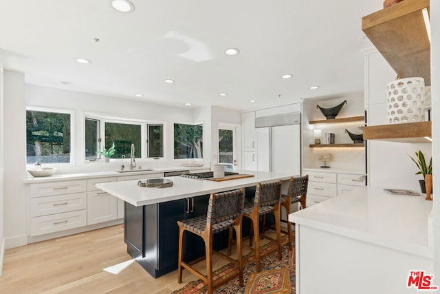 kitchen featuring white cabinets, a kitchen island, sink, light wood-type flooring, and a breakfast bar