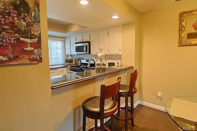 kitchen featuring dark hardwood / wood-style floors, white cabinets, a kitchen breakfast bar, decorative backsplash, and stainless steel appliances