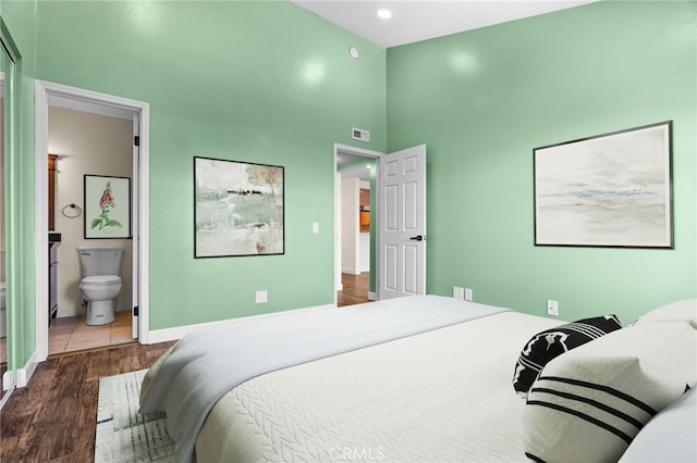 bedroom with a towering ceiling, connected bathroom, and hardwood / wood-style flooring