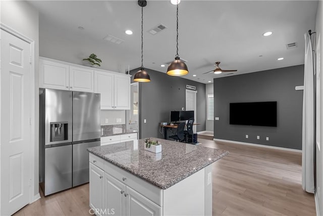 kitchen featuring hanging light fixtures, a center island, stainless steel refrigerator with ice dispenser, light stone counters, and white cabinets