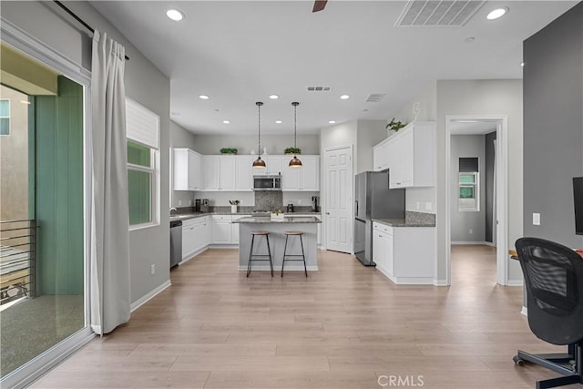 kitchen featuring pendant lighting, white cabinetry, stainless steel appliances, a kitchen breakfast bar, and a kitchen island