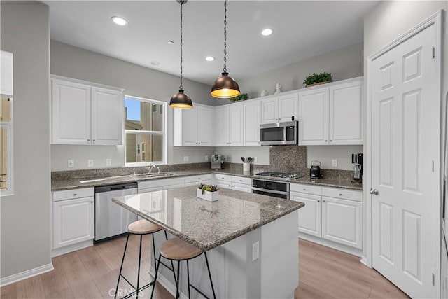 kitchen featuring hanging light fixtures, dark stone countertops, appliances with stainless steel finishes, a kitchen island, and white cabinets