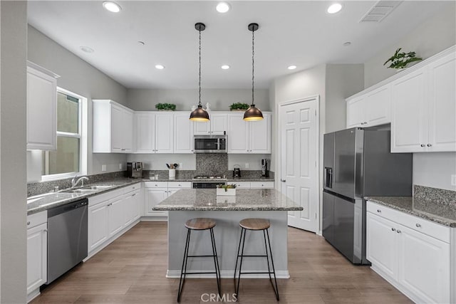 kitchen featuring decorative light fixtures, white cabinetry, sink, a center island, and stainless steel appliances