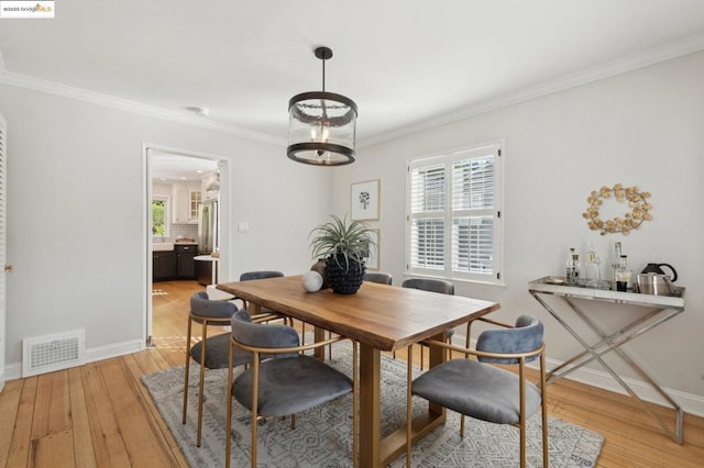 dining room with ornamental molding and light hardwood / wood-style floors