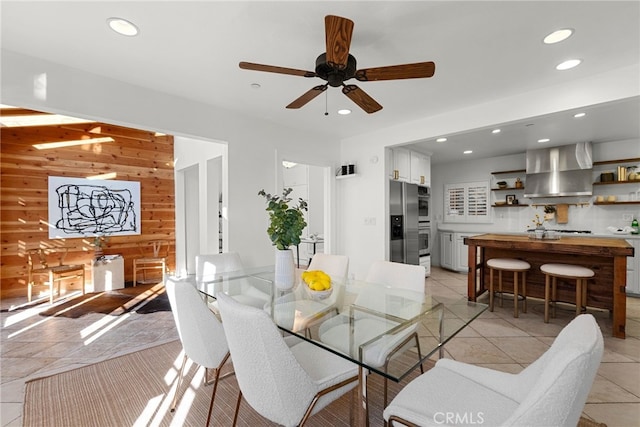 dining area with wooden walls, ceiling fan, and light tile patterned flooring