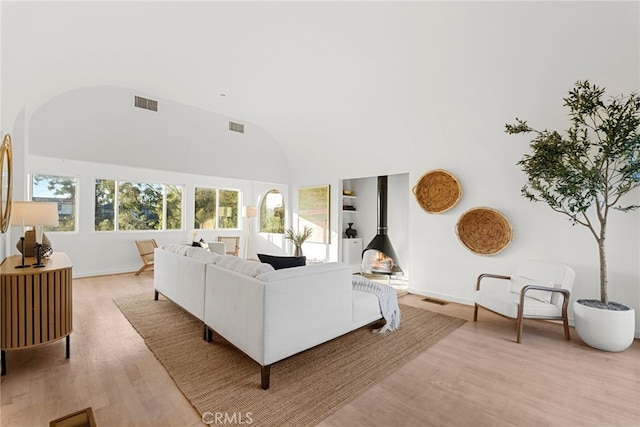 living room featuring vaulted ceiling, a wood stove, and light wood-type flooring