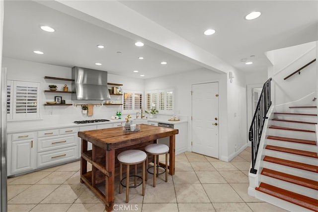 kitchen featuring wall chimney range hood, light tile patterned floors, stainless steel gas stovetop, and white cabinets