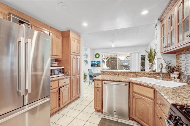 kitchen with appliances with stainless steel finishes, tasteful backsplash, light tile patterned flooring, light stone counters, and sink