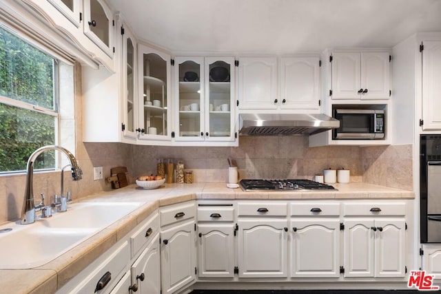 kitchen with tasteful backsplash, tile countertops, sink, white cabinetry, and appliances with stainless steel finishes