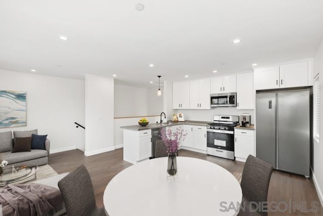 kitchen with decorative light fixtures, white cabinets, kitchen peninsula, and appliances with stainless steel finishes