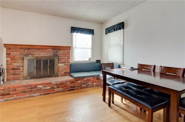 dining room with light hardwood / wood-style floors, a textured ceiling, and a brick fireplace