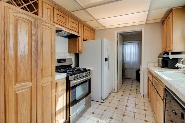 kitchen featuring a paneled ceiling, tasteful backsplash, stainless steel range with gas cooktop, and tile counters