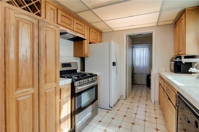 kitchen featuring a paneled ceiling, decorative backsplash, stainless steel range with gas stovetop, and tile countertops