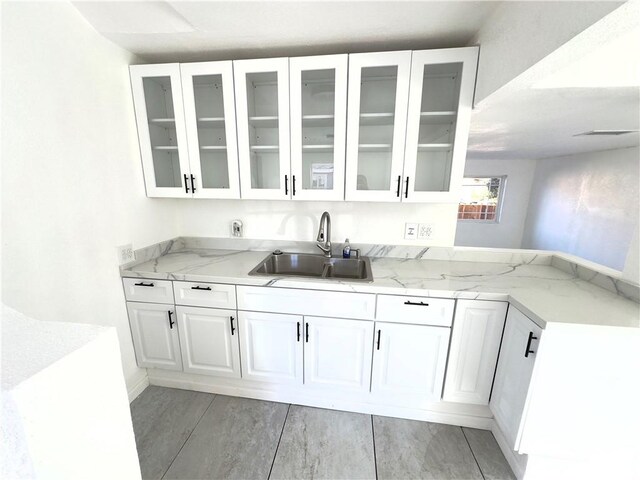 bar featuring white cabinetry, light stone counters, and sink