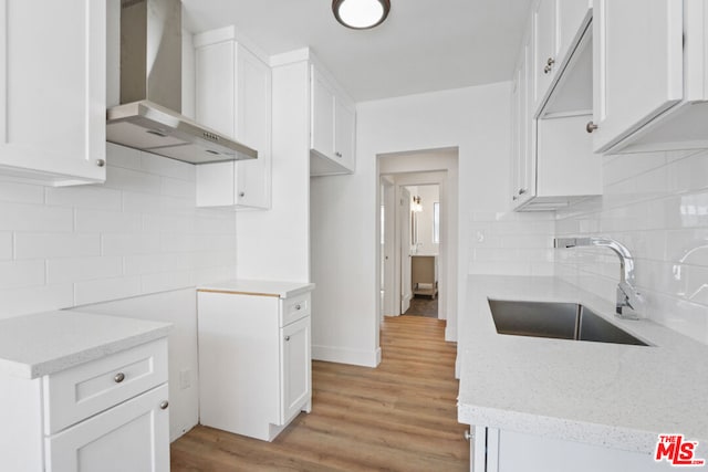 kitchen with light hardwood / wood-style floors, backsplash, wall chimney range hood, white cabinets, and sink