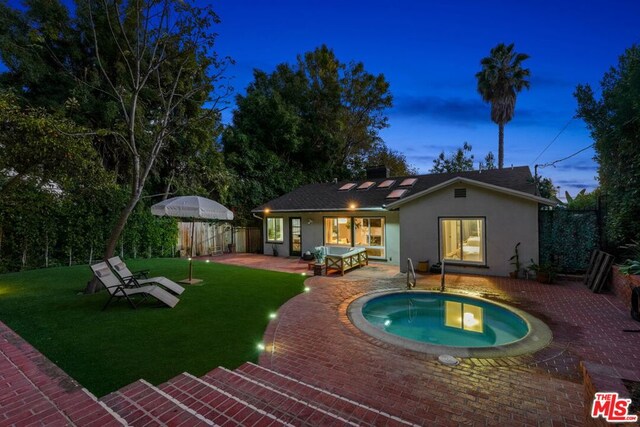 pool at dusk featuring a yard, a jacuzzi, and a patio